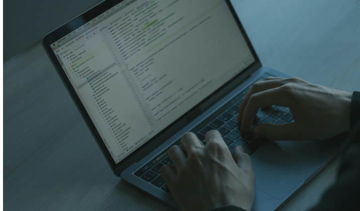 Computer with code and hands typing on the keyboard