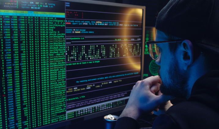 Hacker looking at a computer screen full of code in a dark room