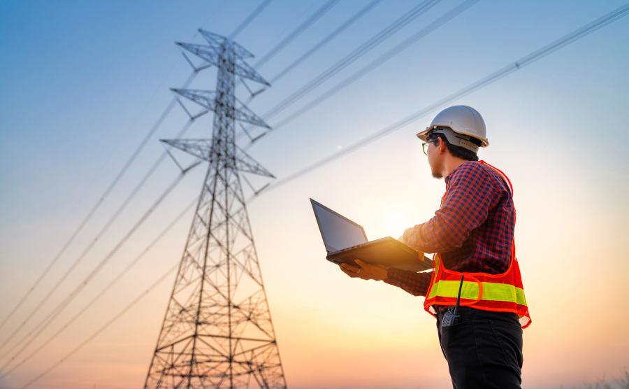 Electrical worker with laptop overlooking power lines